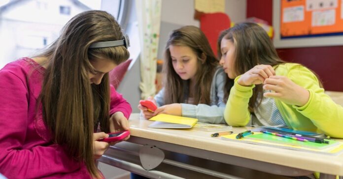 Estudiantes en un aula de escuela secundaria utilizando teléfonos celulares